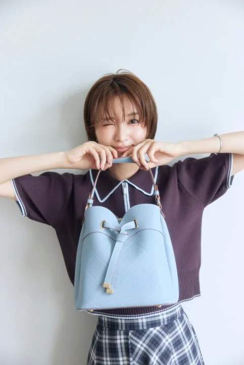 水色のキルティングバケットバッグを持つショートヘアの女性