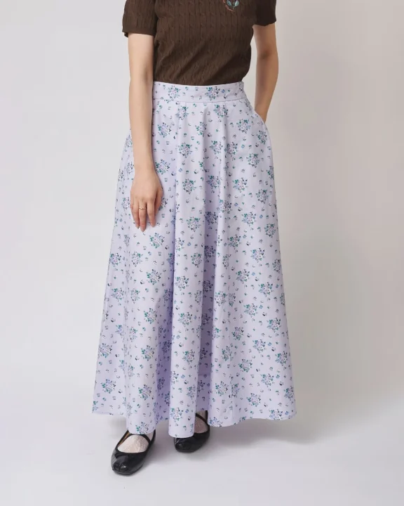 ラベンダー色の小花柄ロングスカートと茶色の半袖トップスを着用した女性