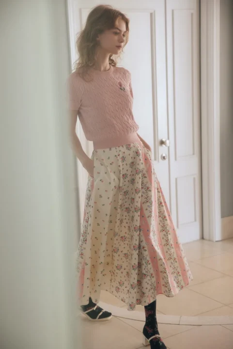 ピンクの半袖ニットと花柄のロングスカートを着用した女性