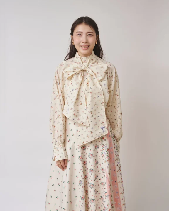 クリーム色の花柄のボウタイブラウスとロングスカートを着用した女性