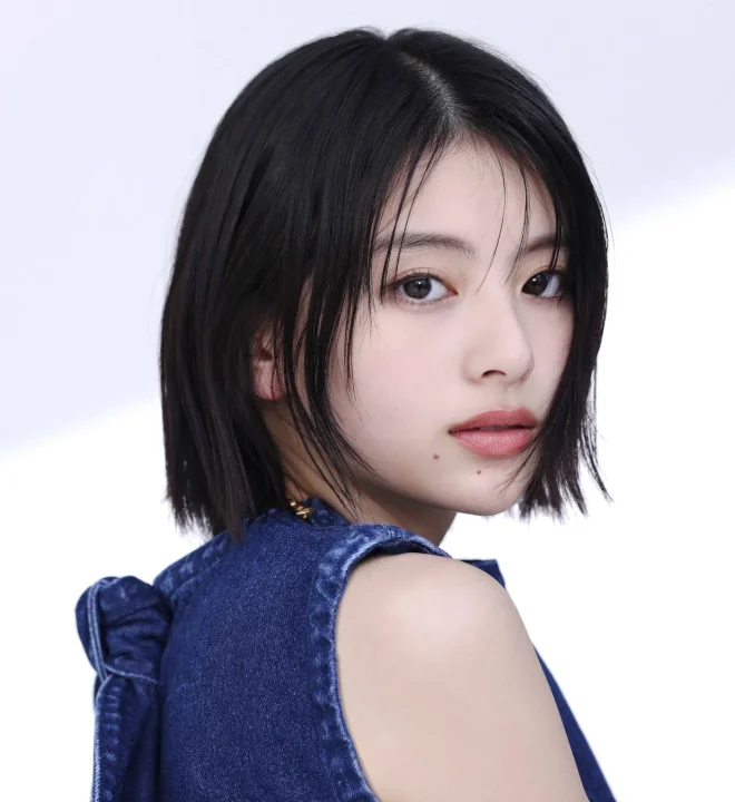 短い黒髪の若い日本人女性が、デニムのトップスを着用し、肩越しにカメラを見つめるポートレート