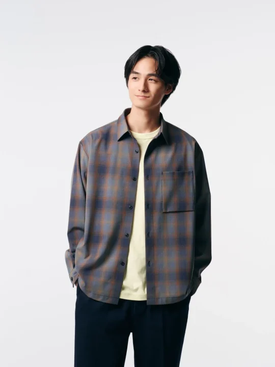 チェック柄の長袖シャツと黄色のTシャツ、紺色のズボンを着用した男性