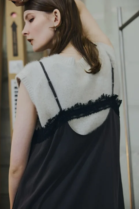 クリーム色ニットベストと黒いレーストリムキャミソールドレスの女性