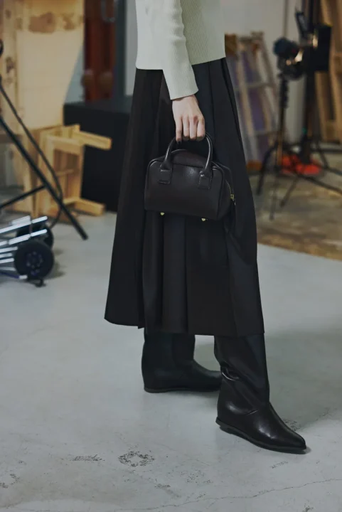 白いニットと黒いプリーツスカート、ミニハンドバッグの女性