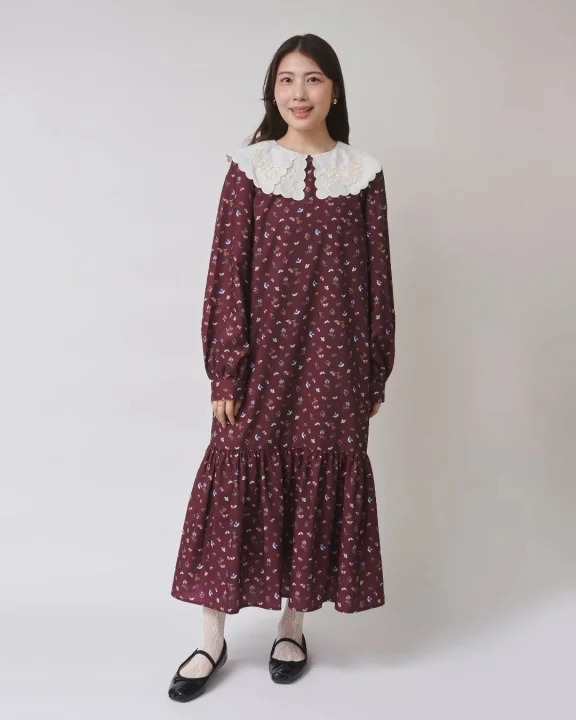 白い刺繍の丸襟が特徴的な、えんじ色の小花柄ロングワンピースを着た女性
