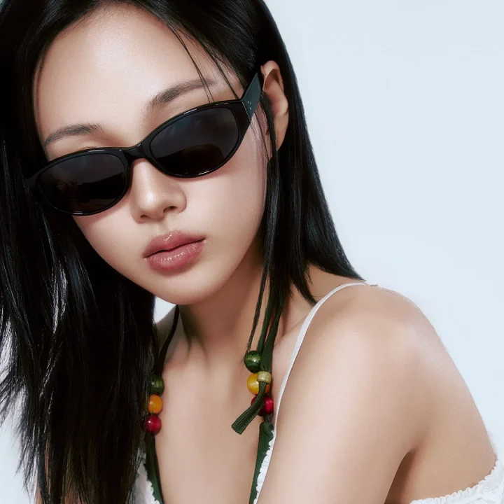 黒いサングラスをかけたアジア人女性のクローズアップポートレートです。長い黒髪が特徴で、白いトップスを着用し、髪にはカラフルなビーズの飾りが付いています。洗練されたクールな雰囲気を醸し出しています。