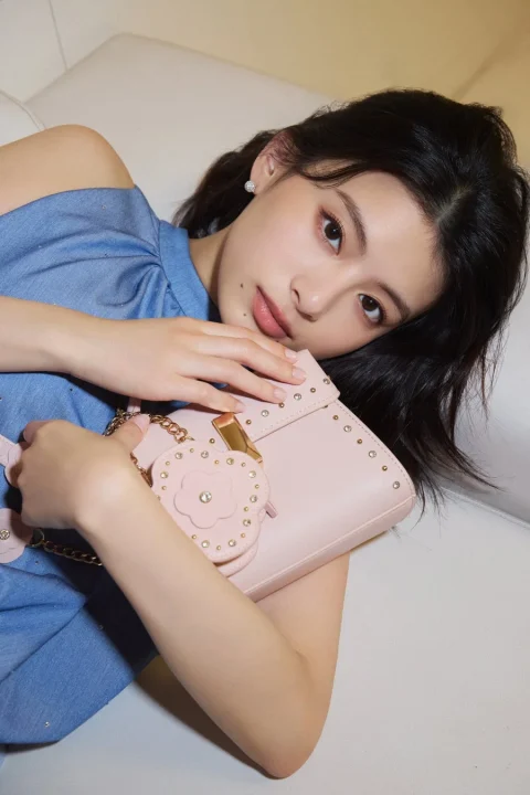 若い女性がピンクのハンドバッグを持ち、水色のトップスとパンツを着用しています