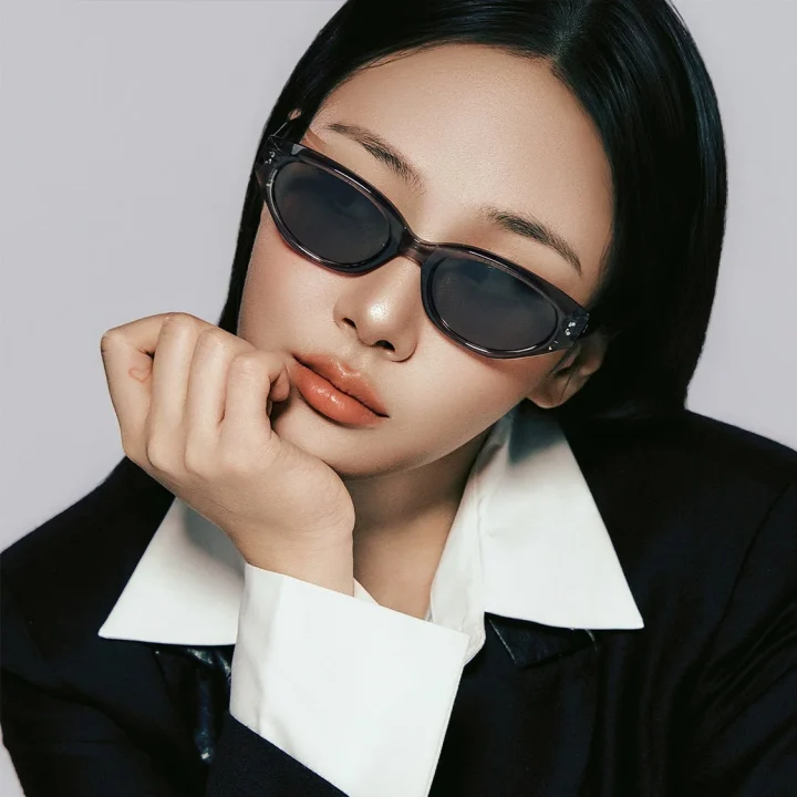 スタイリッシュなサングラスをかけた女性のクローズアップポートレート。黒いブレザーと白いシャツを着用し、顎に手を当てたクールな表情が特徴的で、洗練されたファッションと雰囲気を捉えています。