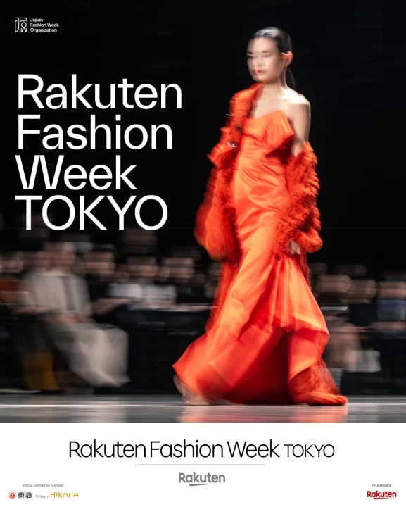 ファッションショーのランウェイを歩くモデルを捉えた画像です。鮮やかなオレンジ色のドレスとコートを身につけたモデルが印象的で、「Rakuten Fashion Week TOKYO」のプロモーションビジュアルとして使用されているようです。