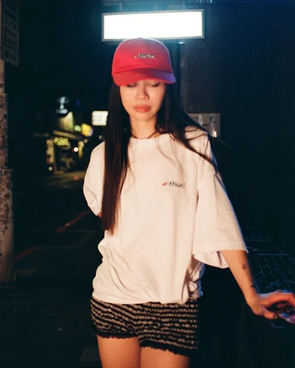 夜の街角に立つ赤いキャップと白いTシャツの女性