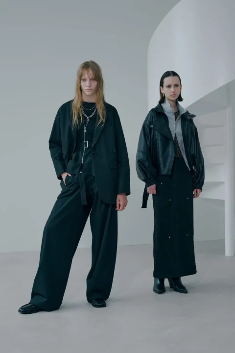 ミニマルな白いスタジオで撮影された、ダークトーンのオーバーサイズな服をまとった2人のモデル。