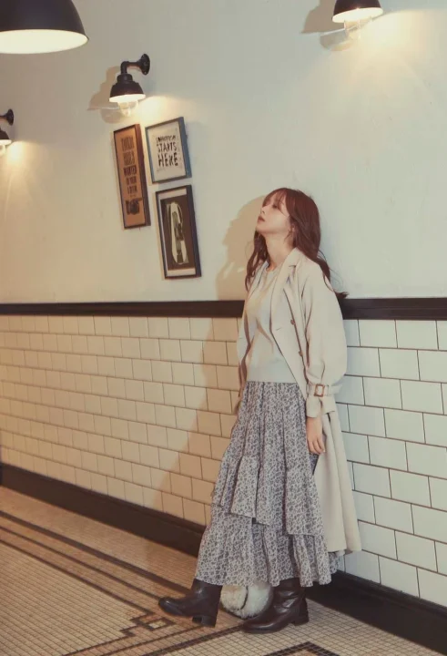 ベージュのトレンチコートと花柄のティアードスカートを着用した女性