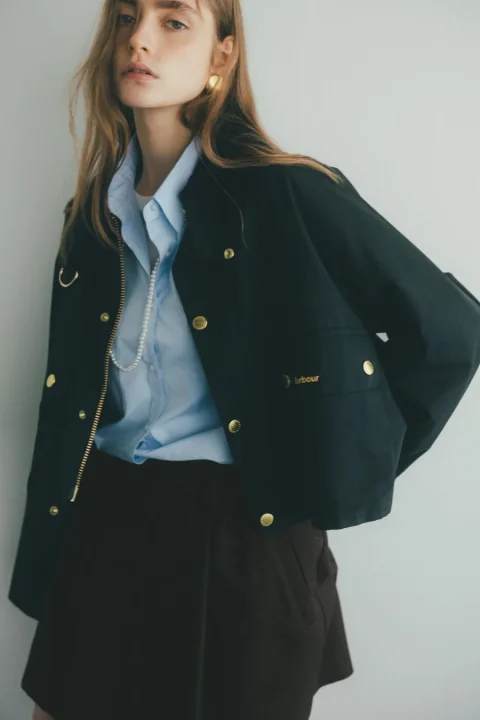 黒いショート丈ジャケットと水色シャツを着用した女性