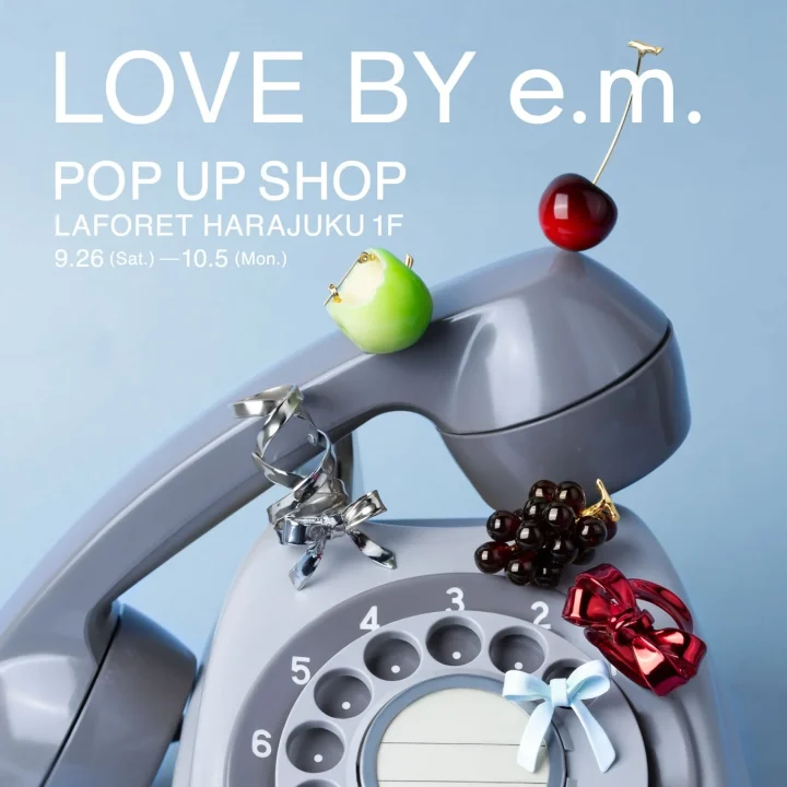 レトロなダイヤル式電話機の上に、フルーツやリボンを模したアクセサリーが飾られた、e.m.のポップアップショップ開催を告知する画像